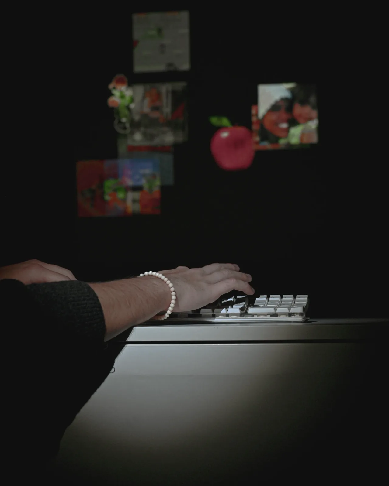 Hands typing on a lit keyboard in a dark room, images projected on the wall behind