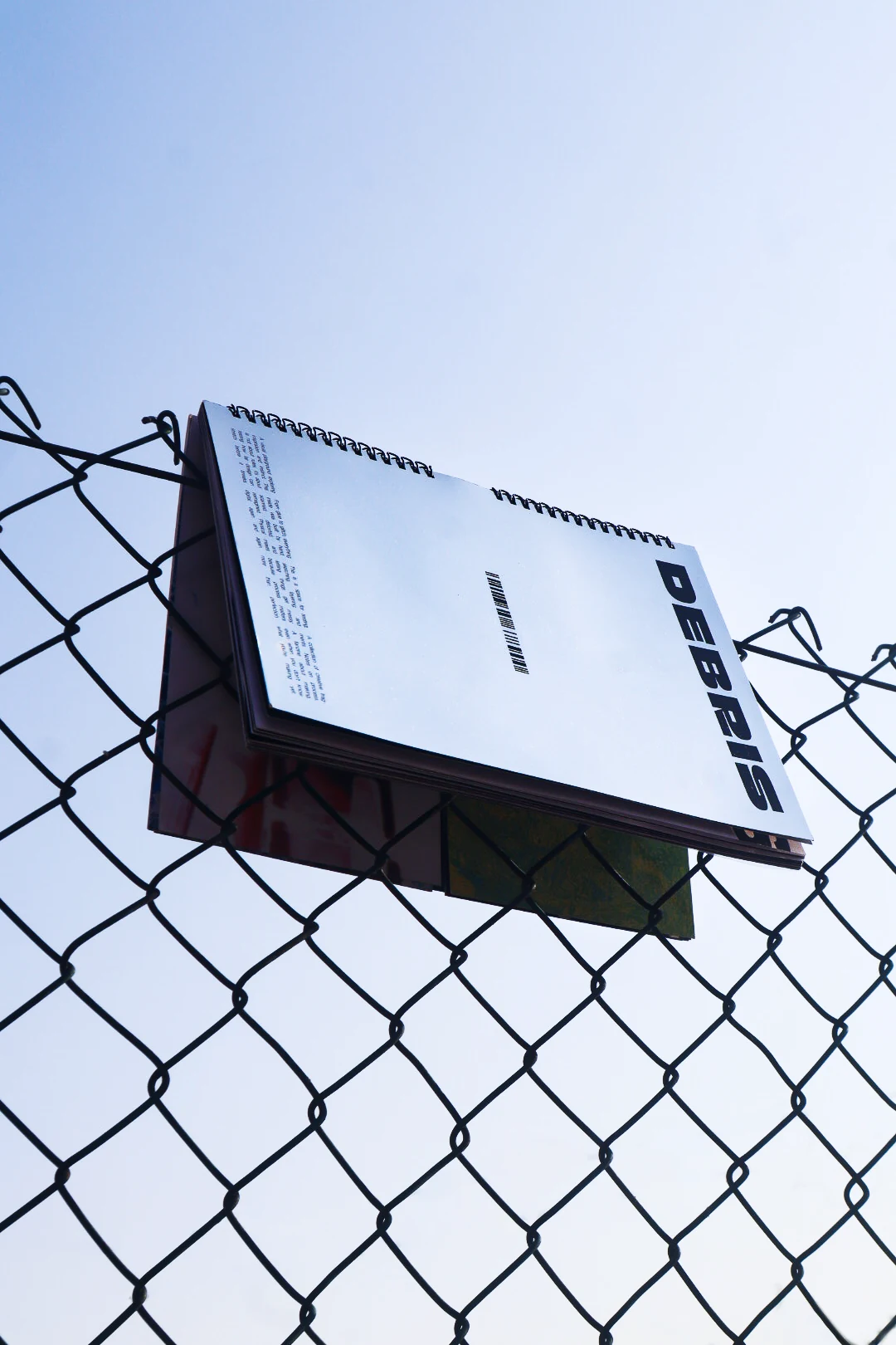 The magazine hooked onto a chain-link fence against an open sky